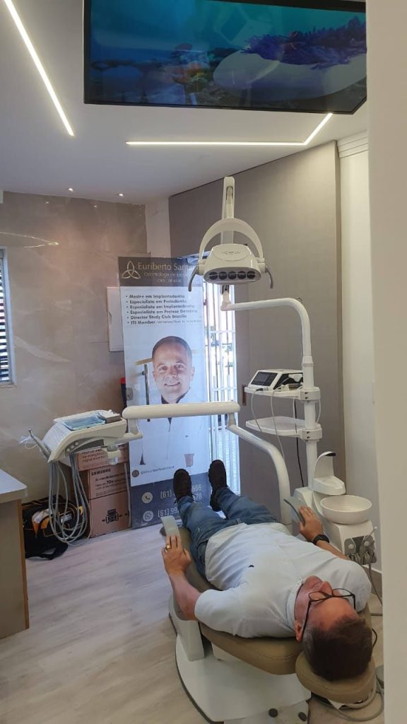 Paciente na cadeira odontológica assistindo TV instalada no teto do consultório em Brasília